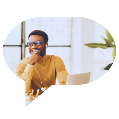 Homem sorridente usando fones de ouvido durante uma videoconferência no escritório, com laptop aberto e planta decorativa ao fundo.